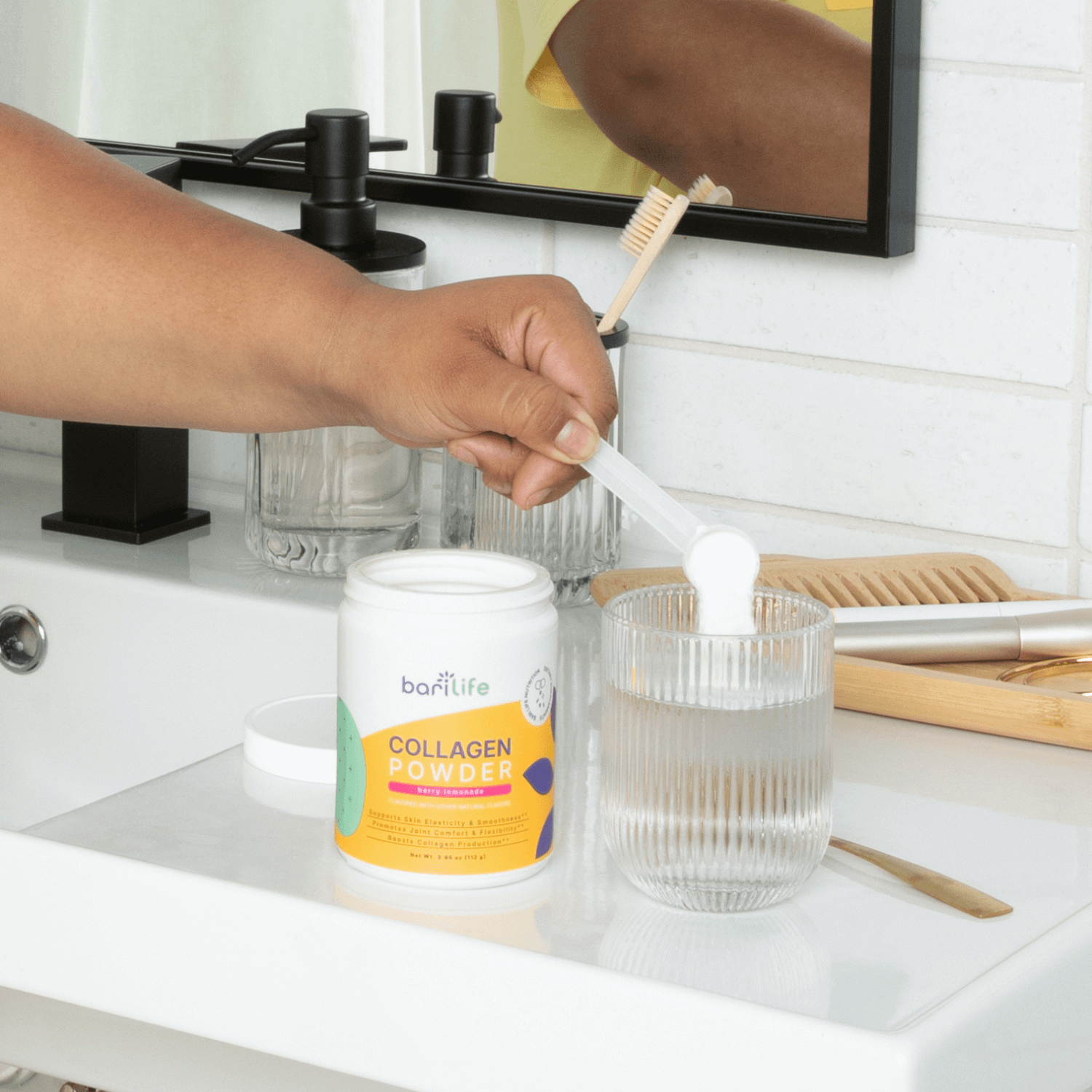 Hand adding Bariatric Collagen Powder to a glass of water at a bathroom counter, promoting wellness.